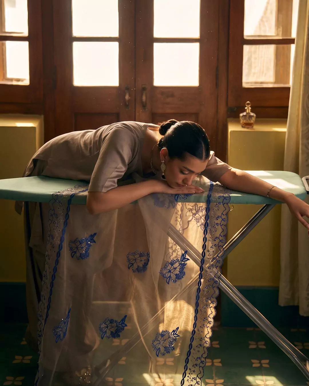 KALZARII 2026 formalwear editorial featuring a model in a light blue outfit photographed beside an ironing board