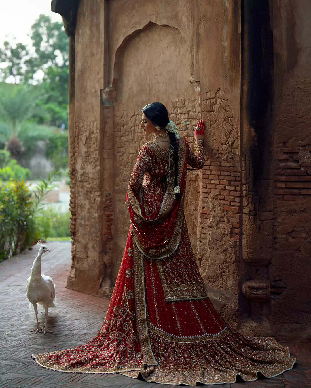 Back view of a bridal attire showcasing the extended embroidered train and long braid in a vintage Lahore setting.