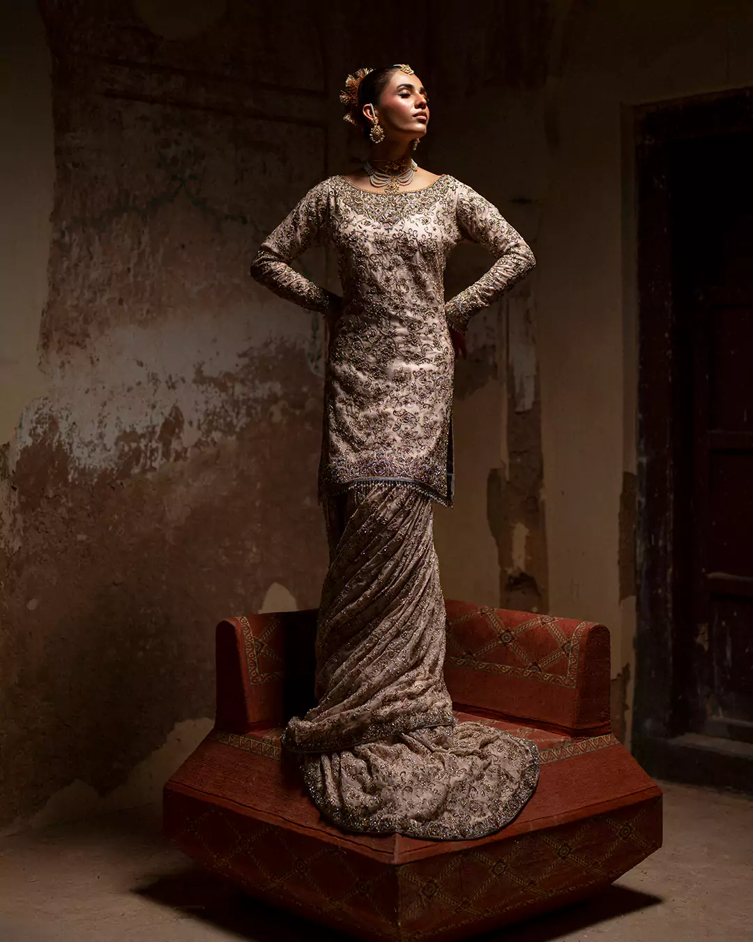 Model standing on a vintage stool wearing a structured ivory and silver metallic embroidered jacket-style outfit.