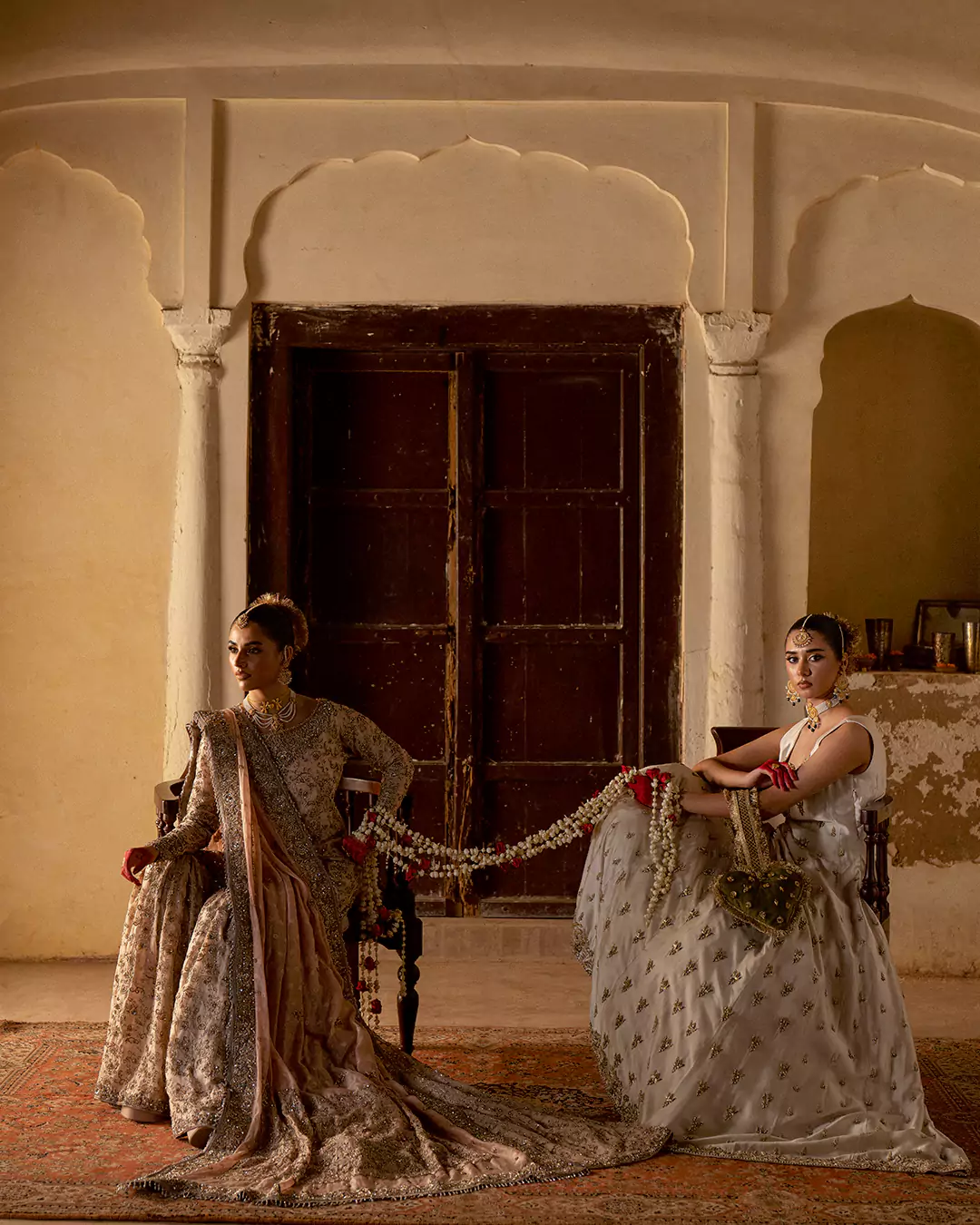 Two models in ivory and soft champange bridal wear connected by a floral rose garland in an architectural hall.