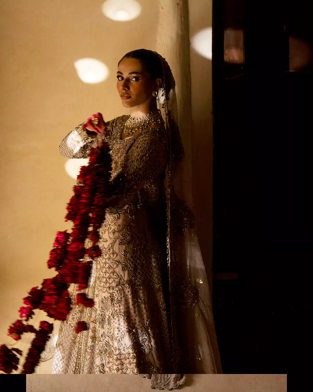 Close-up portrait of a model wrapped in an embellished ivory veil with motion-blurred red rose garlands.