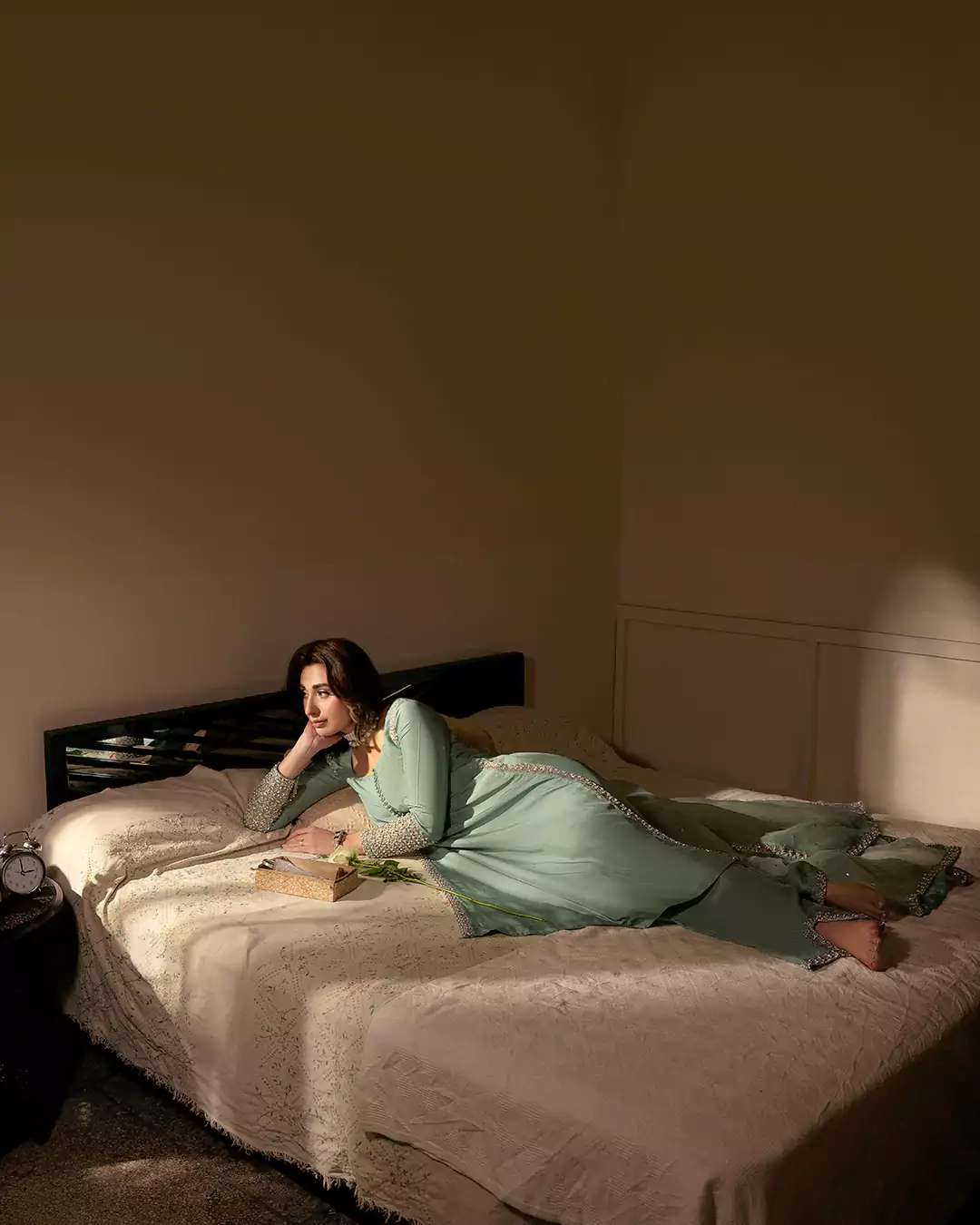 Model wearing a light-green outfit while lying on a bed for the AKKS by Attya Luxury Pret 2025 campaign.