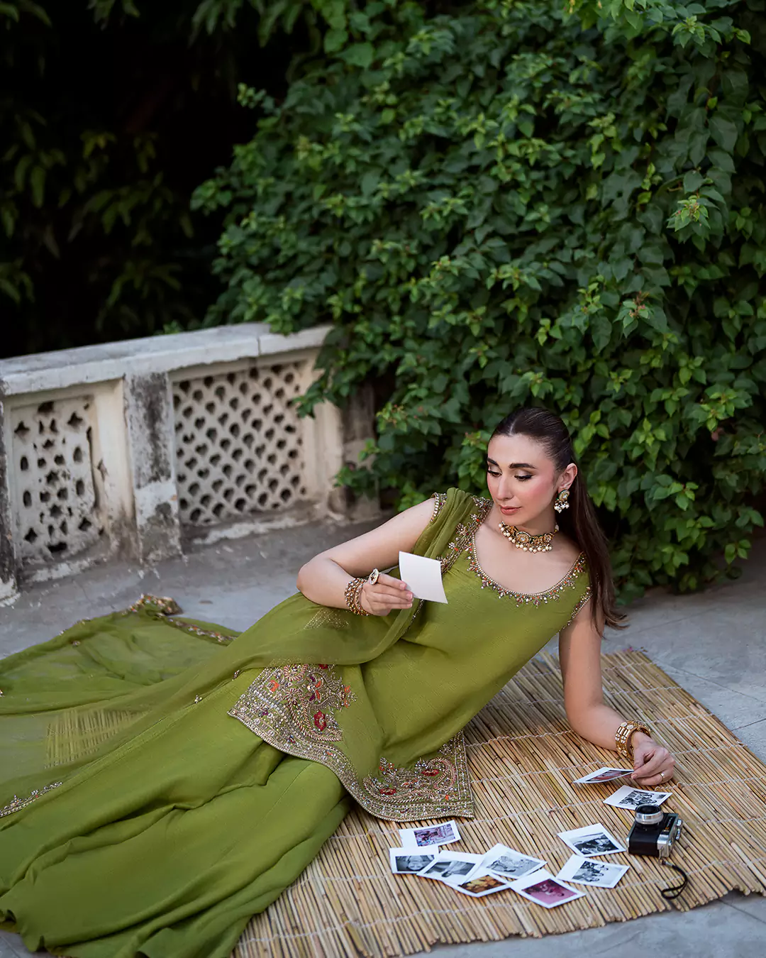 Model wearing a green outfit while lying on a traditional chitai roof covering and looking at a photograph, with printed pictures arranged nearby.